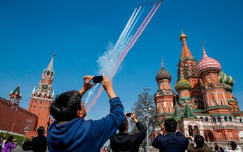 Tourists take pictures with their mobile phones as Russian Su-25 assault aircrafts release smoke in the colours of the Russian flag while flying over Red Square during a rehearsal for the Victory Day military parade in Moscow on May 4, 2018