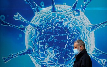 A man wearing a mask walks past a mural of a coronavirus