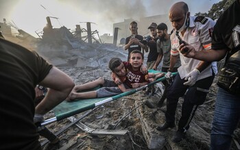 Palestinians carry wounded brothers on a stretcher after recovering them from the rubble of a destroyed area following Israeli air strikes in Gaza City